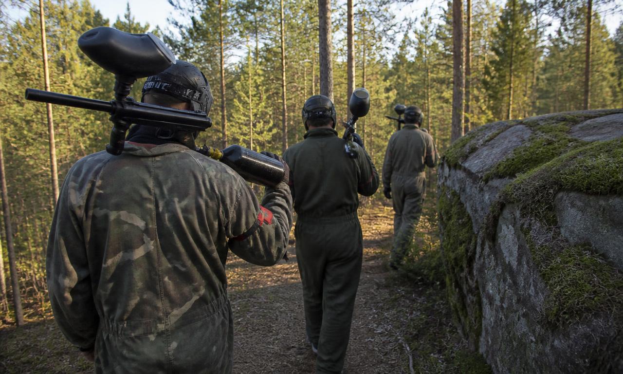 Kolme paintball-pelaajaa kävelee metsäpolulla markkerit olalla.